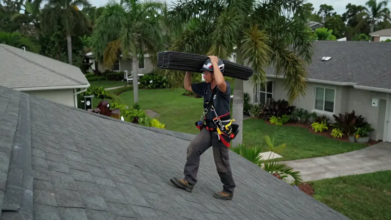 Roof Repair in Sunrise: roofer, wearing a safety harness, is securely walking across a residential shingle roof, carrying a