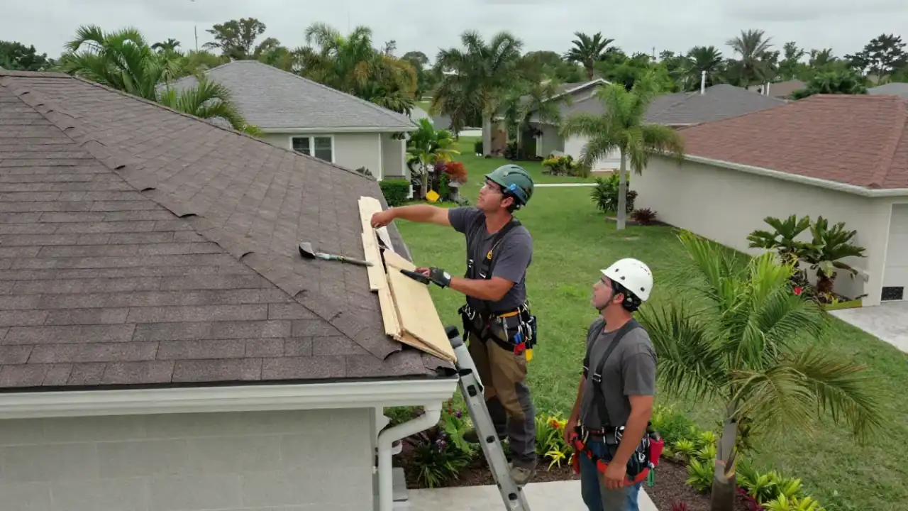 Roof Repair in Sunrise: roofer on a ladder is pointing to a section of loose fascia board on a residential home while